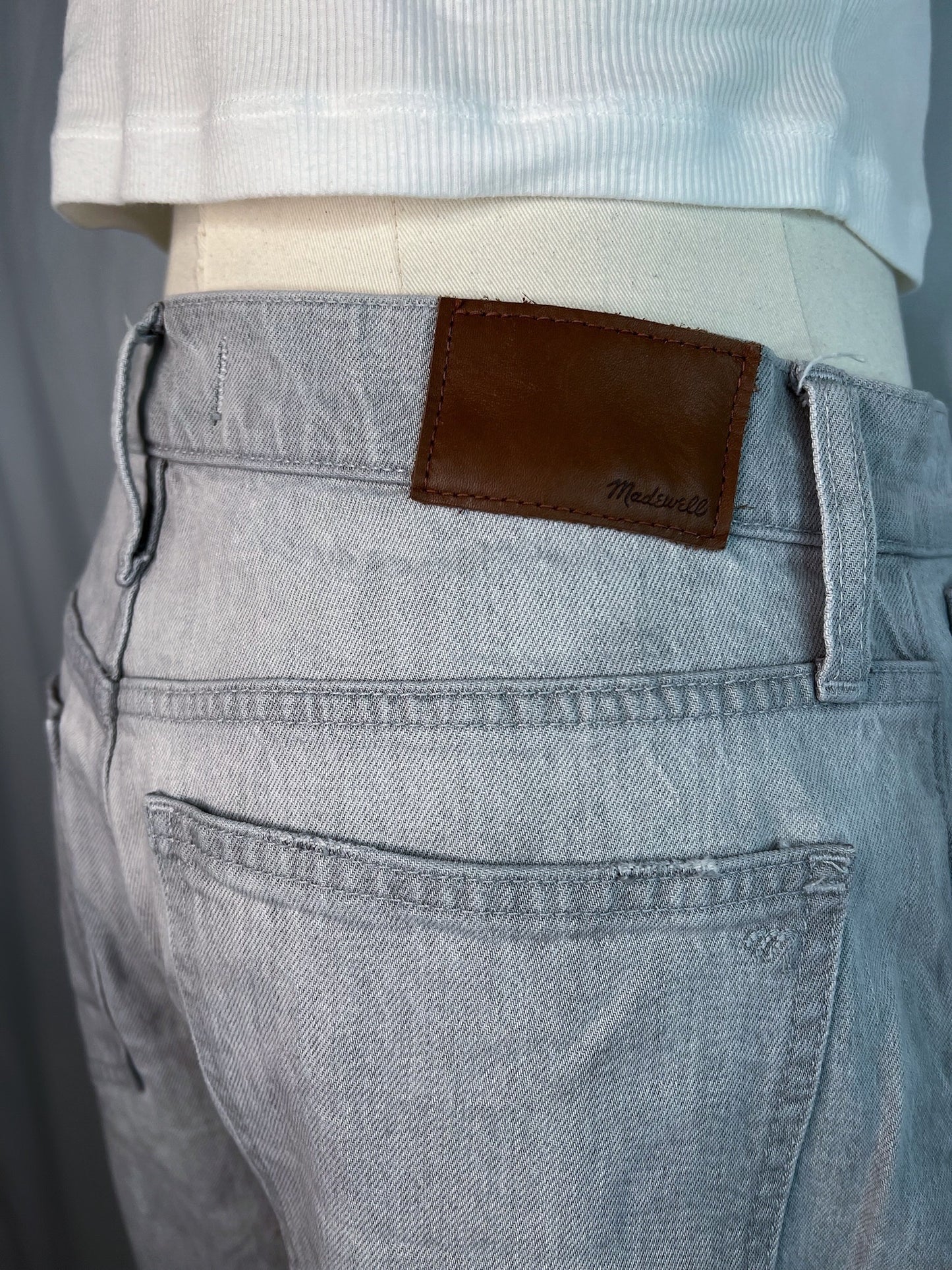 Close up of backside of grey Madewell slim demi-boot jeans featuring the Madewell brown leather tag.