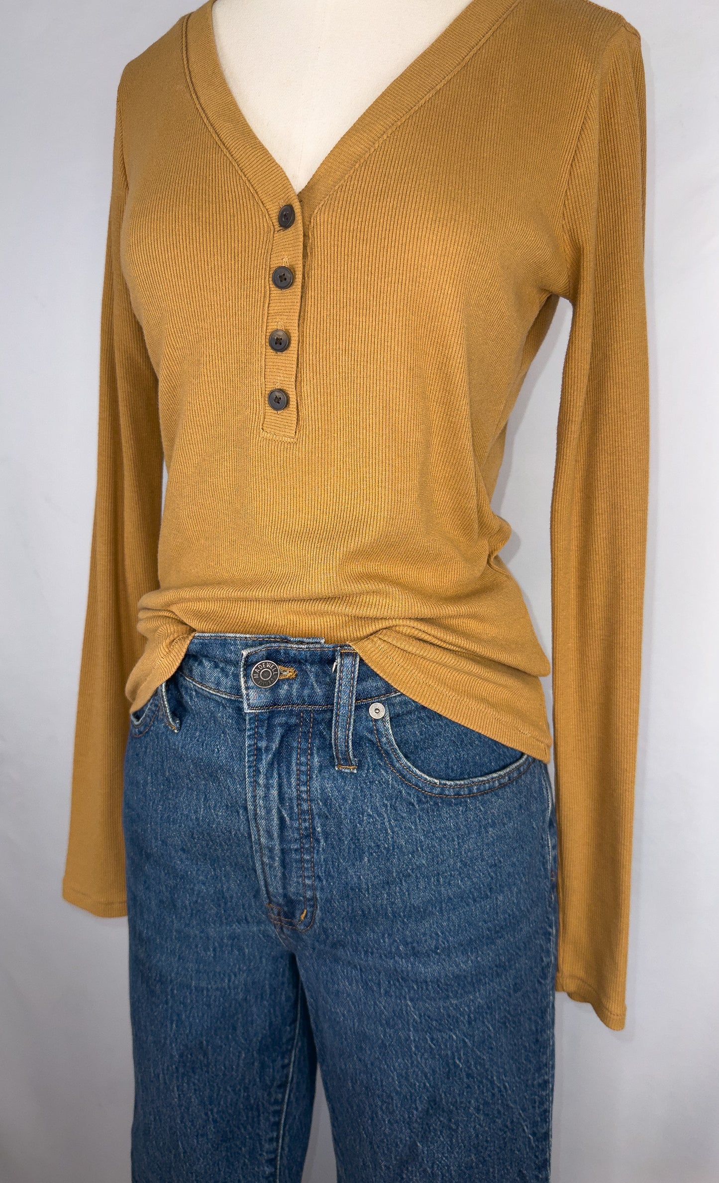 Up-close side view of Madewell Fine Ribbed Henley Tee in Toffee featuring the four small round brown buttons. Top is paired with a dark blue jean.