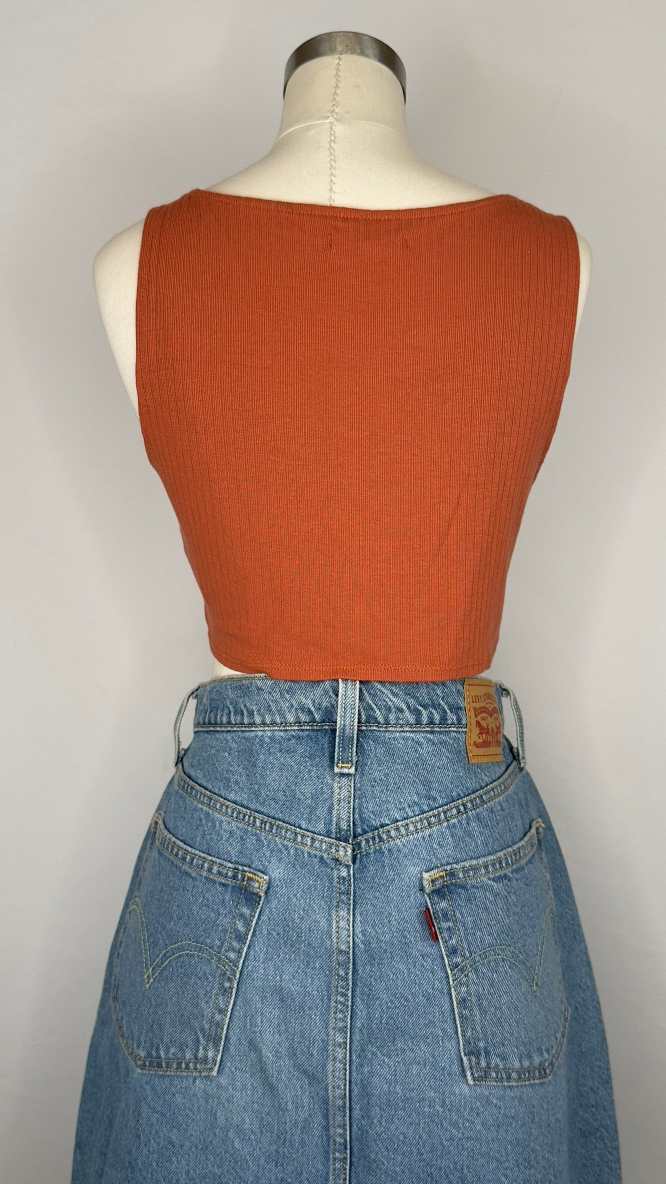 Mannequin wearing a rust-colored sleeveless top and blue jeans on a white background.