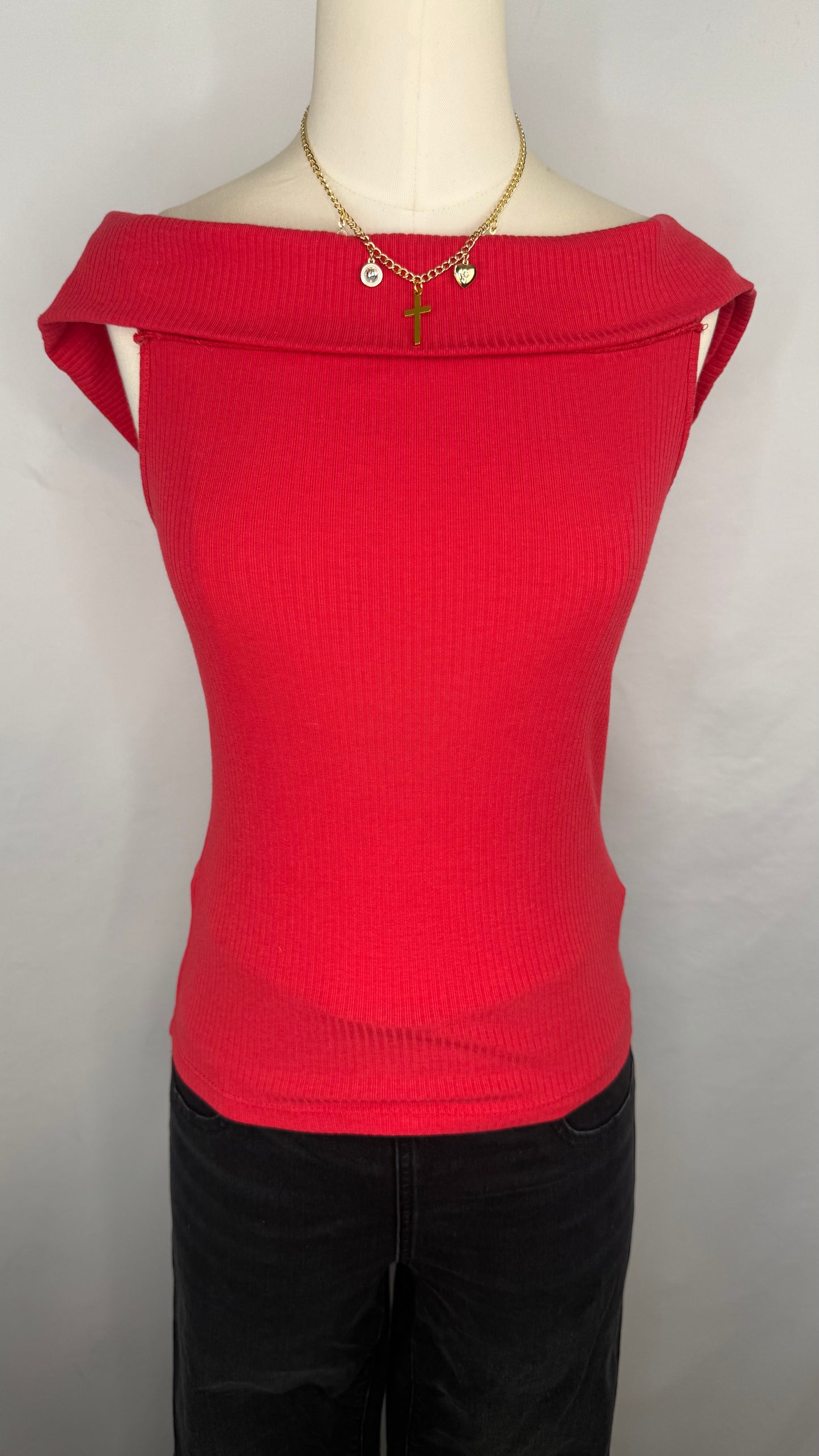 A red, off-shoulder ribbed top displayed on a mannequin with black pants and a necklace.