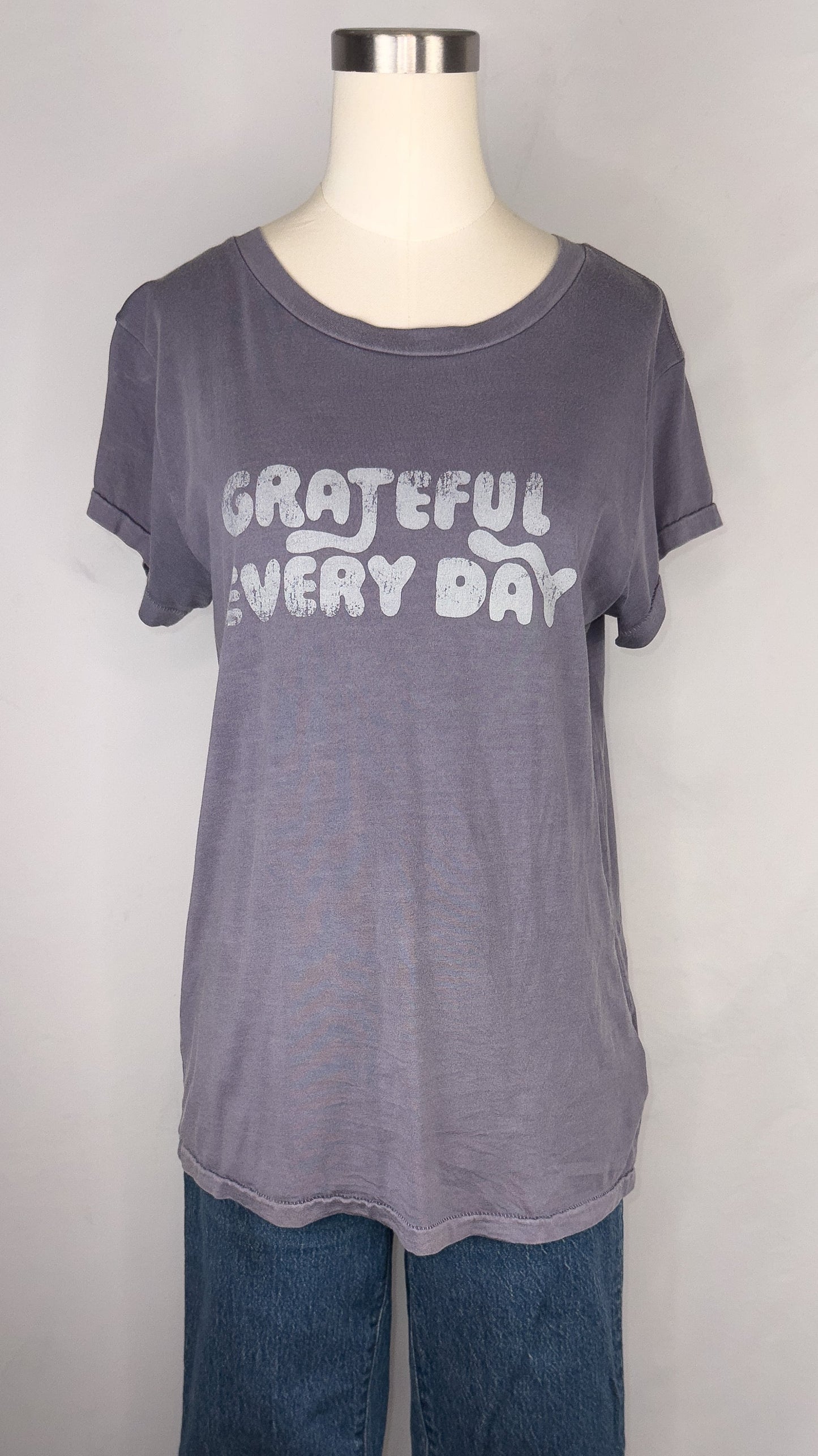 Up-close front facing view of Rivet & Thread Grateful Everyday Graphic Ex-Boyfriend Tee in Sunfaded Indigo, highlighting the distressed-ish letters that read "Grateful Every Day". A dark blue jean is shown paired with the t-shirt