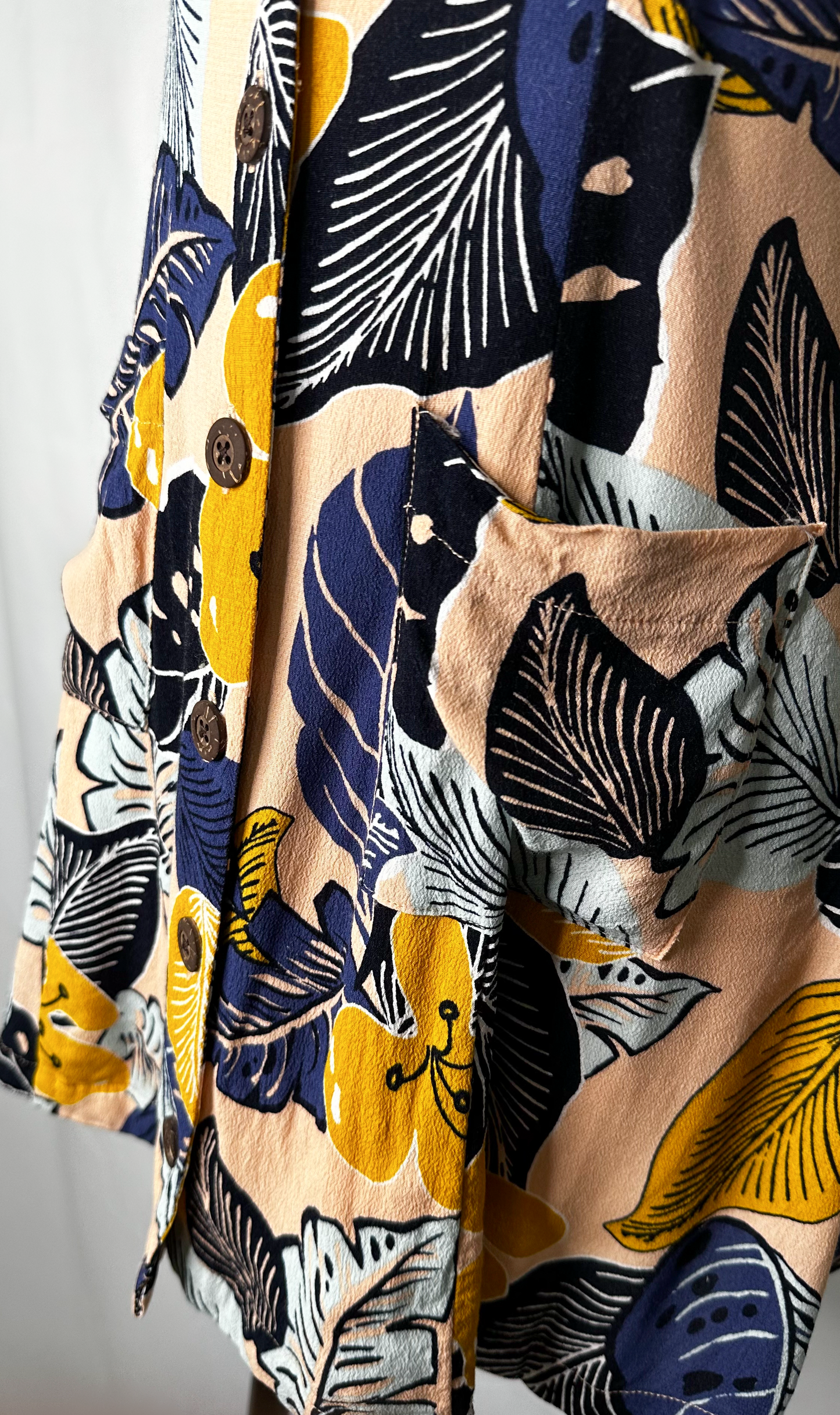 Up-close front side view of Silence + Noise Button-Down Mini Dress in Tropical Print, featuring one of the pockets and some of the wood-like buttons.