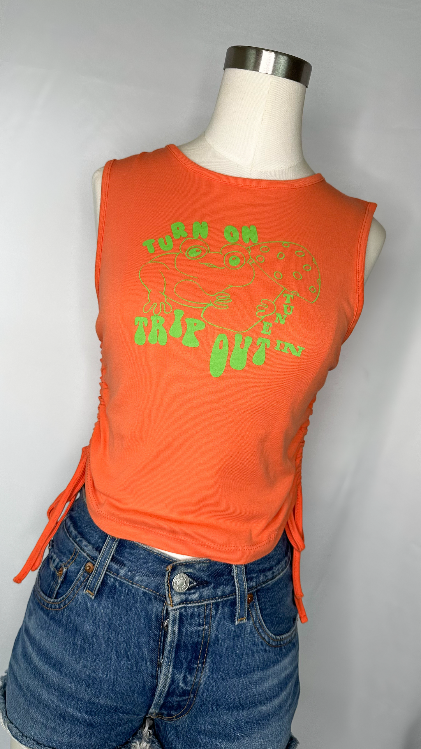 Front Shot of Urban Outfitters Turn On Tune In Crop Top in Bright Orange size large featuring a lime green frog with a mushroom on the front of the shirt.