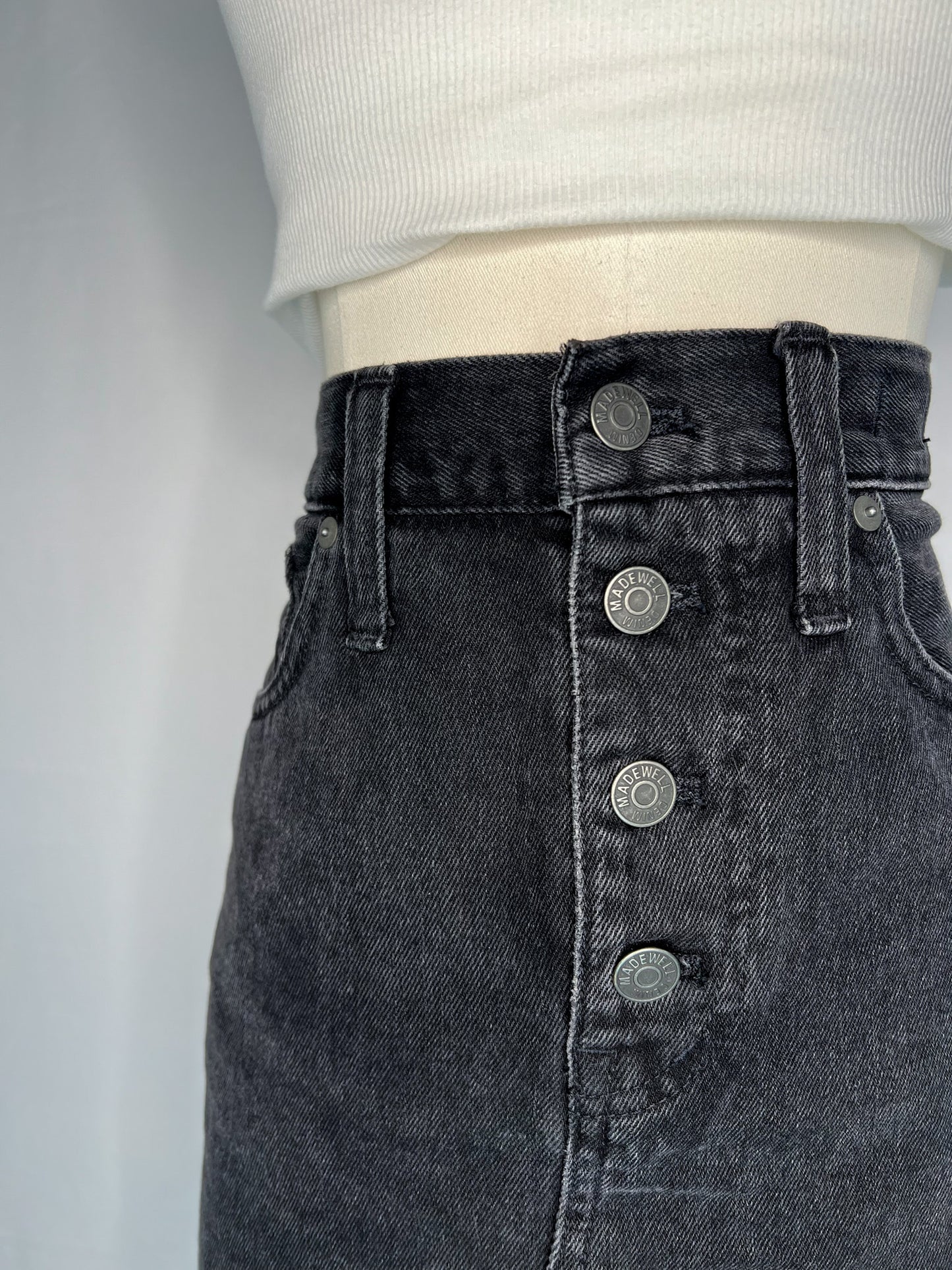 Close up view of Madewell Rigid Denim A-Line Mini Skirt in Lunar Wash: Button-Front Edition, featuring belt loops and button-front.