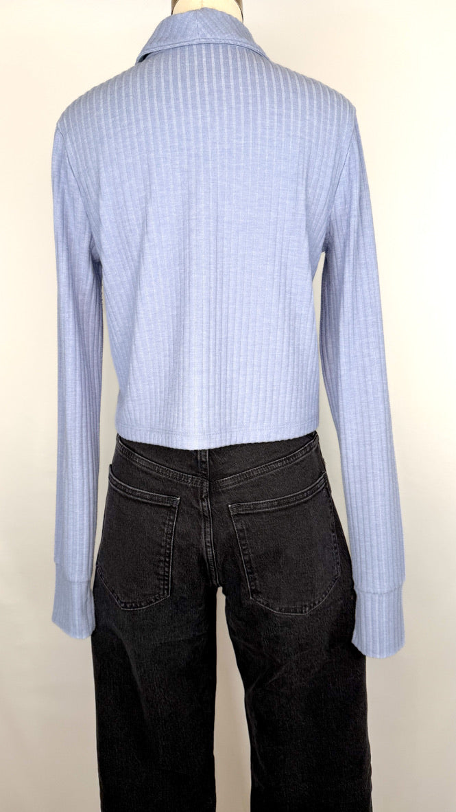 Back view of periwinkle blue ribbed long-sleeve shirt on a mannequin with black jeans against a white background.