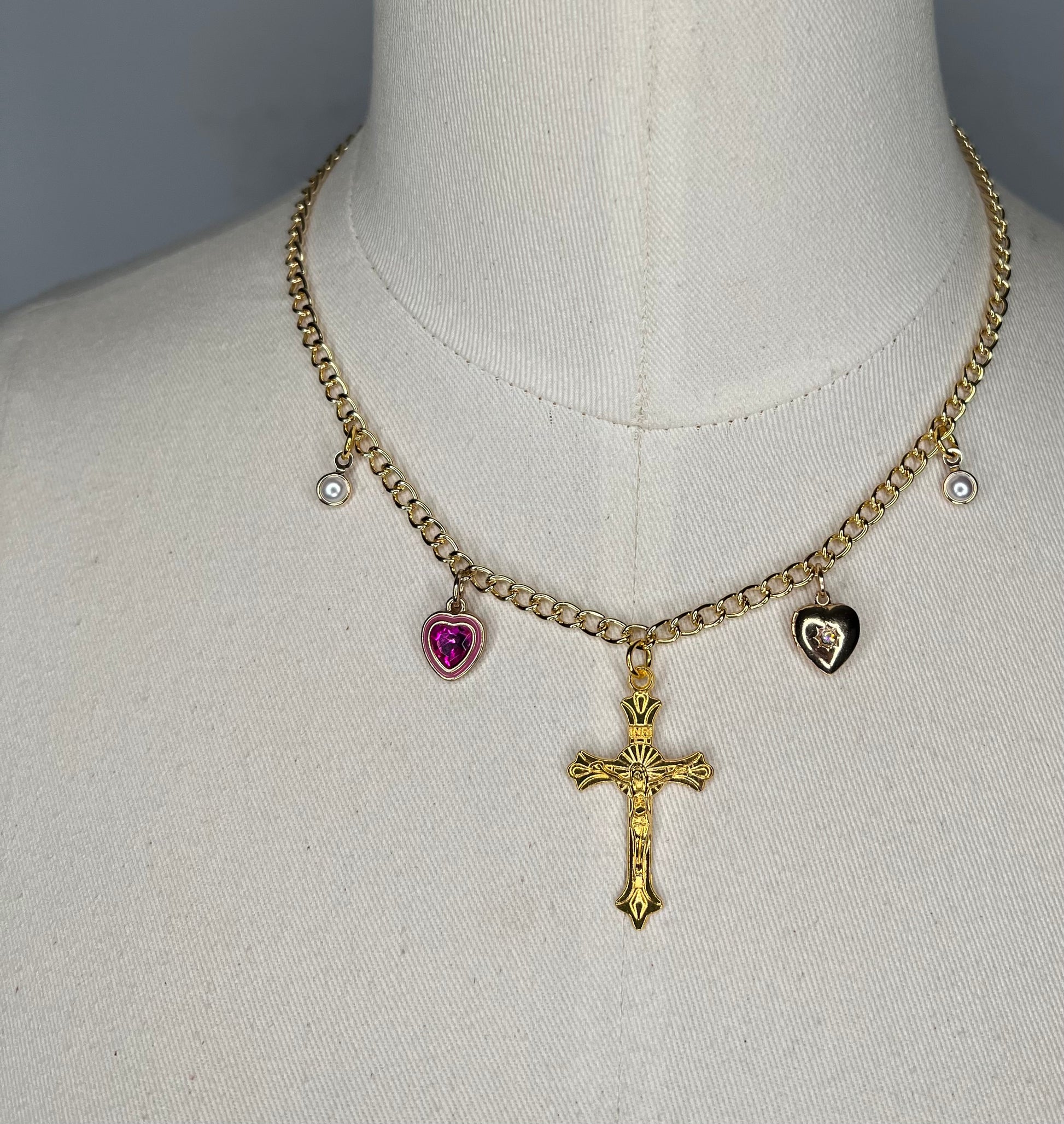 Gold chain necklace with cross charm in the middle, along with four other various charms.