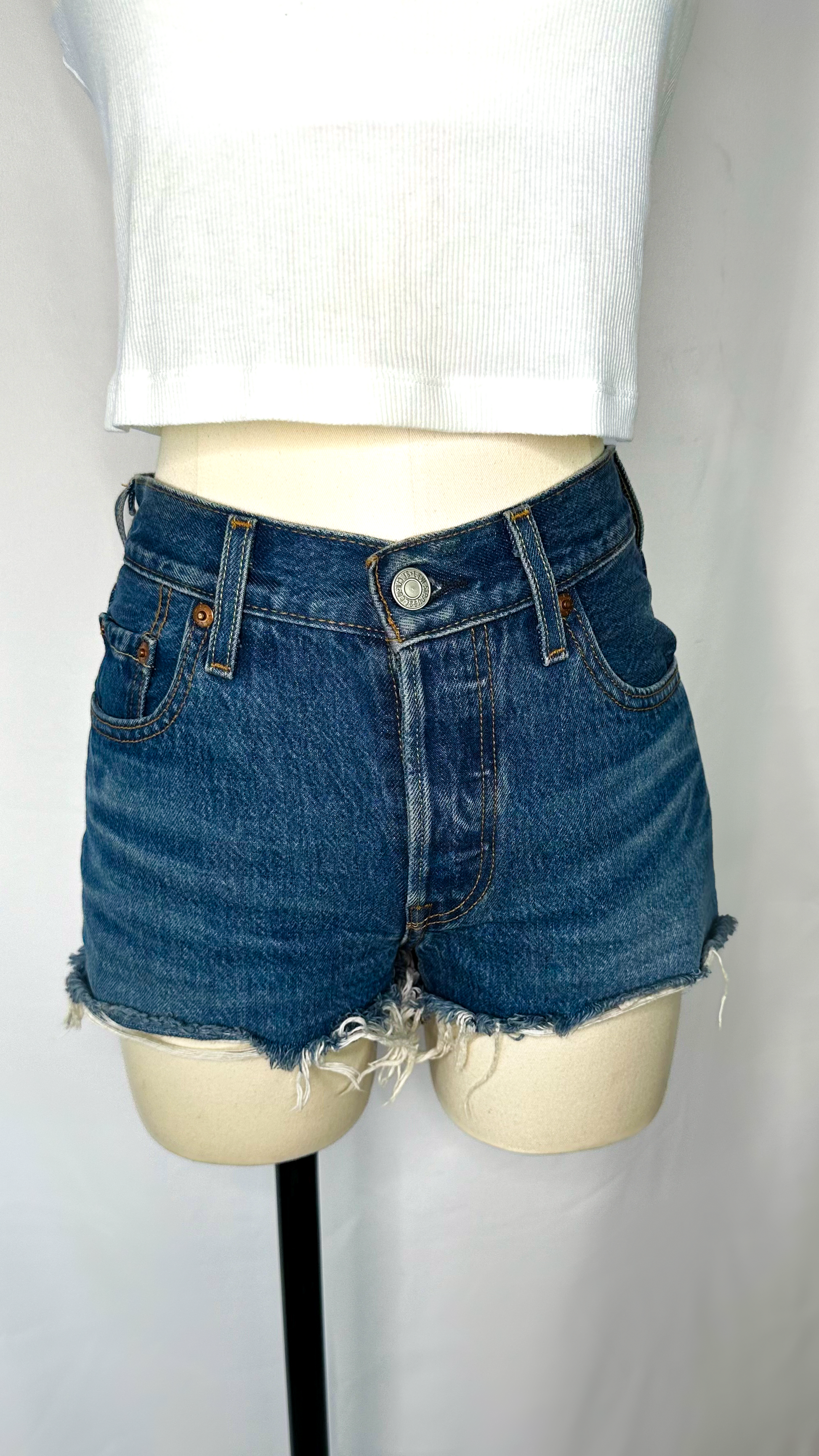 Front shot of Levi's 501 high rise women's shorts in dark wash size 25, featuring a frayed/raw hem and button fly. 