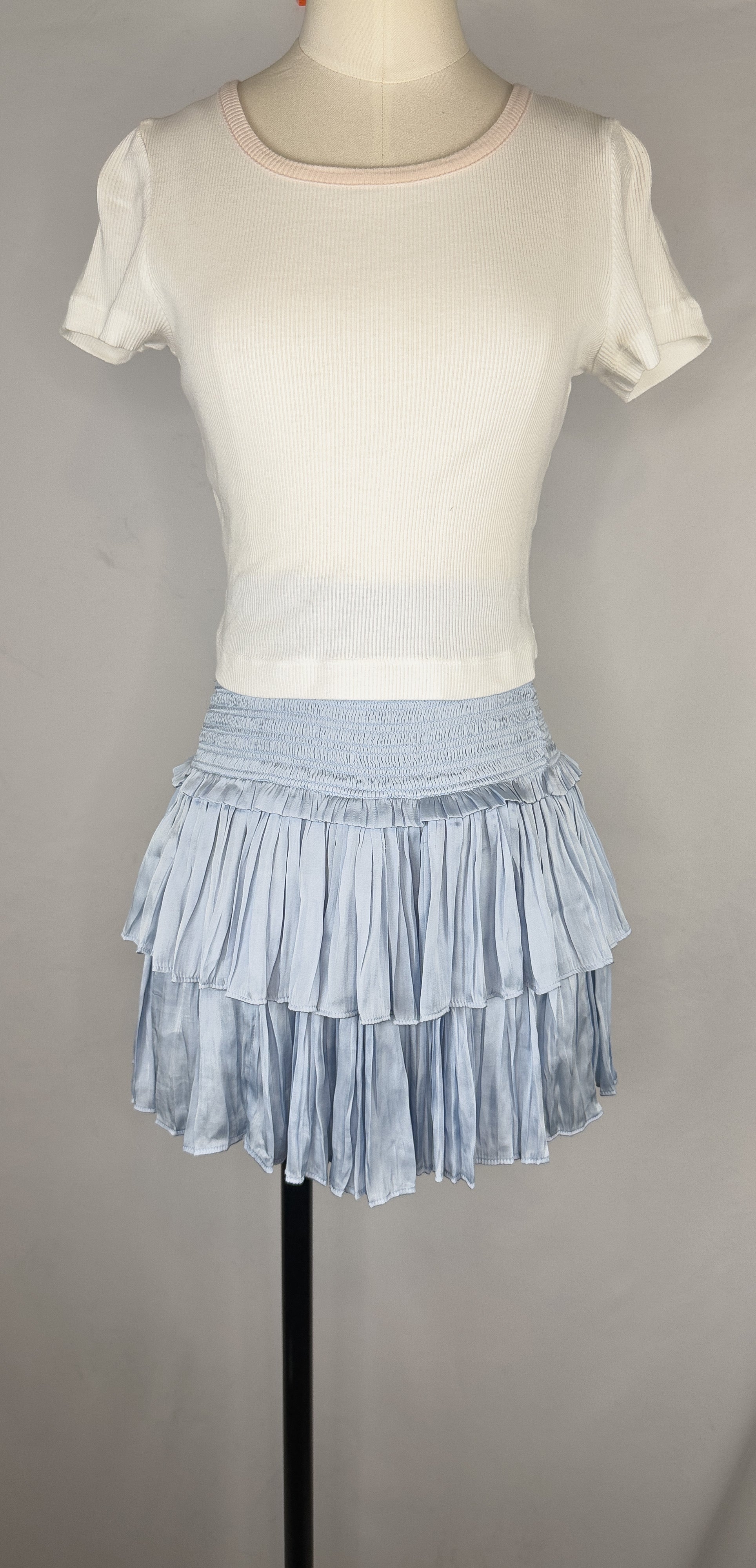 Front view of Reset By Jane Silky Smocked Skirt in Light Blue. The skirt has a smocked waistband and two flouncy layers. The skirt is paired with a cropped white tee.