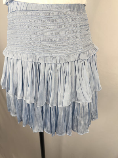 Up-close side view of Reset By Jane Silky Smocked Skirt in Light Blue. The skirt has a smocked waistband and two flouncy layers. The skirt is paired with a cropped white tee.