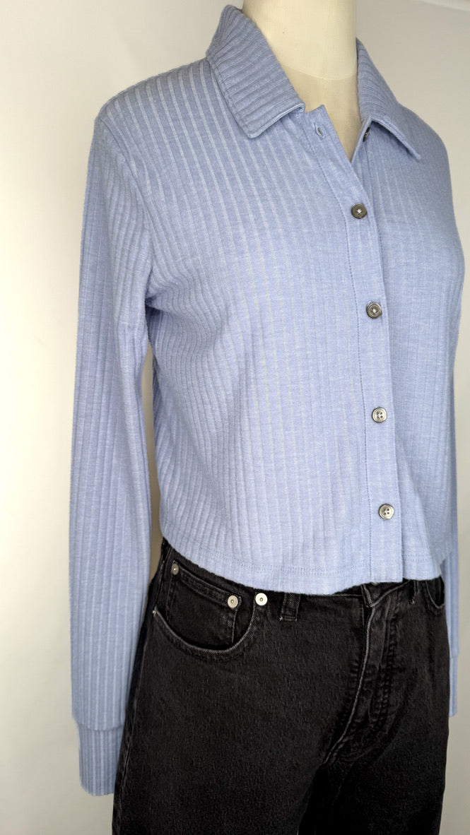 Side view of periwinkle blue button-up shirt on a mannequin with black jeans against a white background.