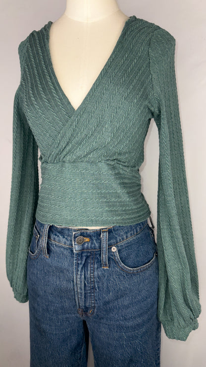 Up-close angle of ZAFUL Ribbed Knit Cropped Wrap Top in Green. This picture highlights the knit detailing on the top. It is again paired with a dark blue jean.